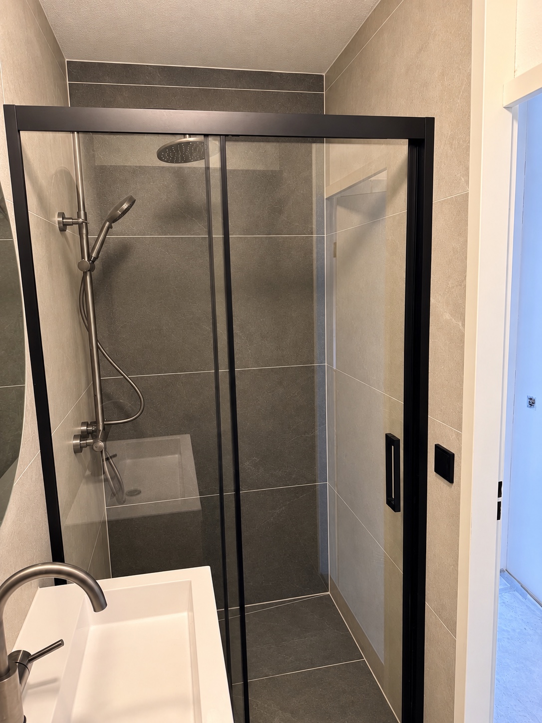 Zwart omlijste douche met steentinten en een deel van de wastafel in Katwijk aan Zee