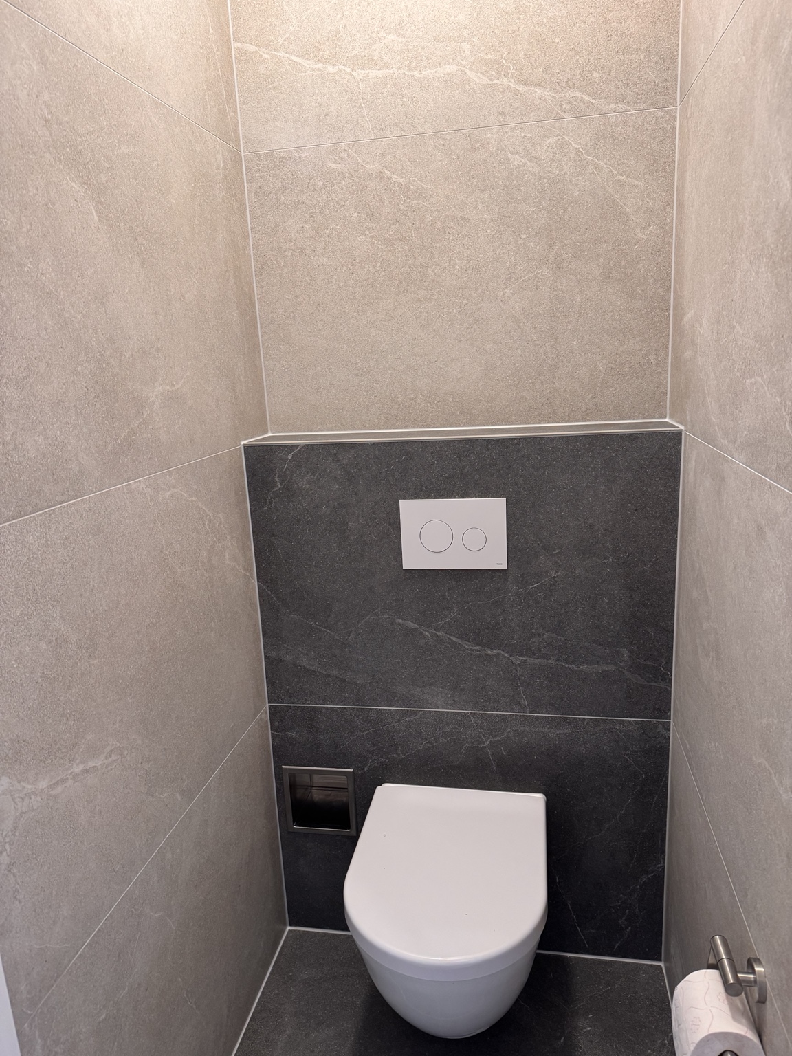 Gerealiseerde aparte toiletruimte in Katwijk aan Zee met wit wandcloset, donkere achterwand en lichte wandtegels